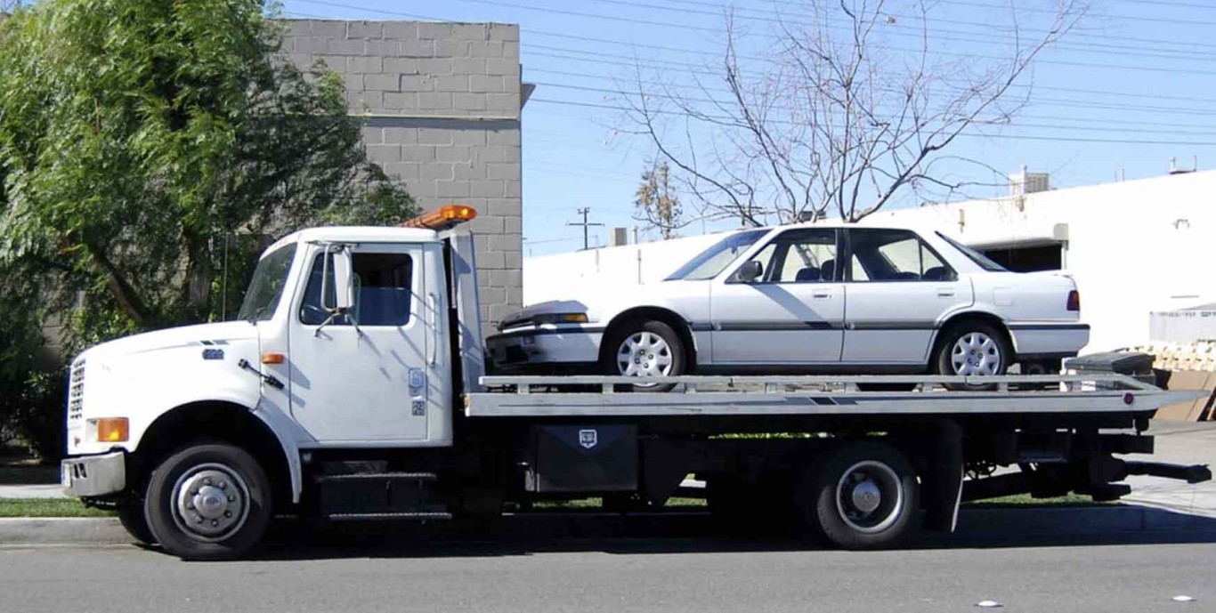 Professional flatbed tow truck carrying a white car in Copiague, NY