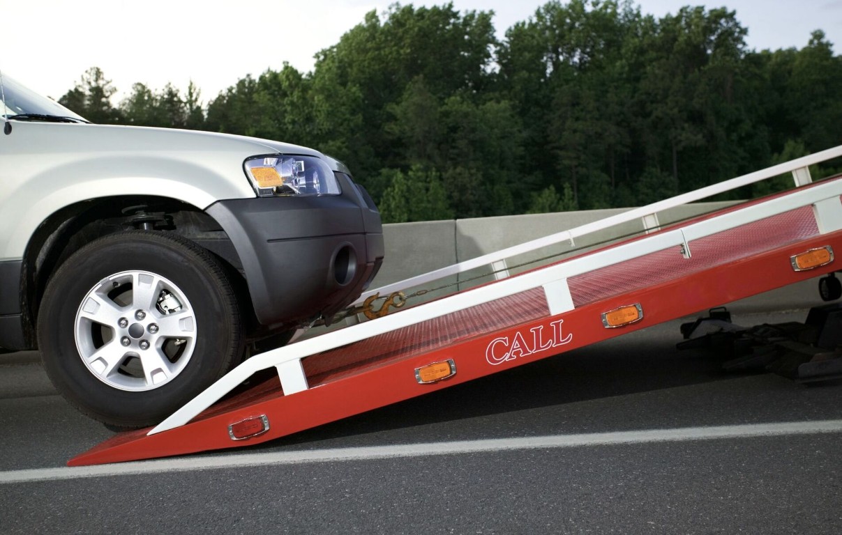 Red flatbed tow truck loading a black SUV at a residential driveway in Copiague, NY